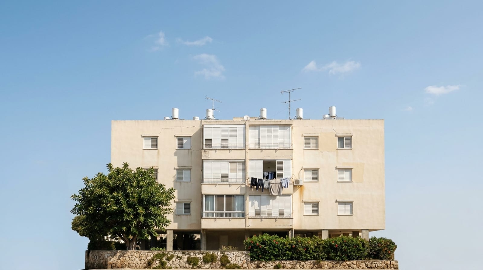 בניין שיכון ותיק מול שמיים כחולים, דודי שמש ואנטנות על הגג, כביסה במרפסת