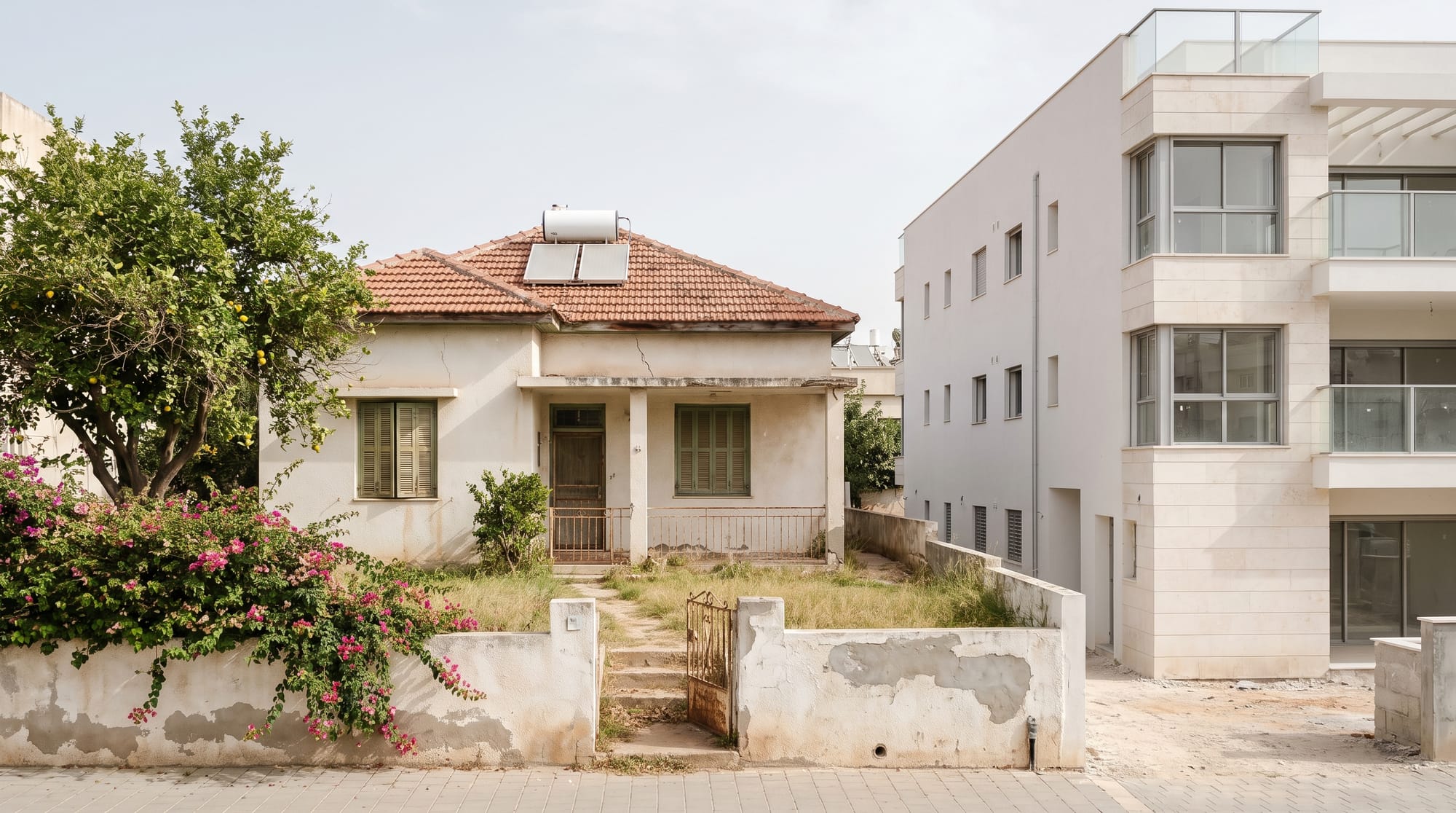 Ein altes eingeschossiges Haus mit Ziegeldach in einem großen Garten, daneben auf dem Nachbargrundstück ein neues, höheres Wohngebäude