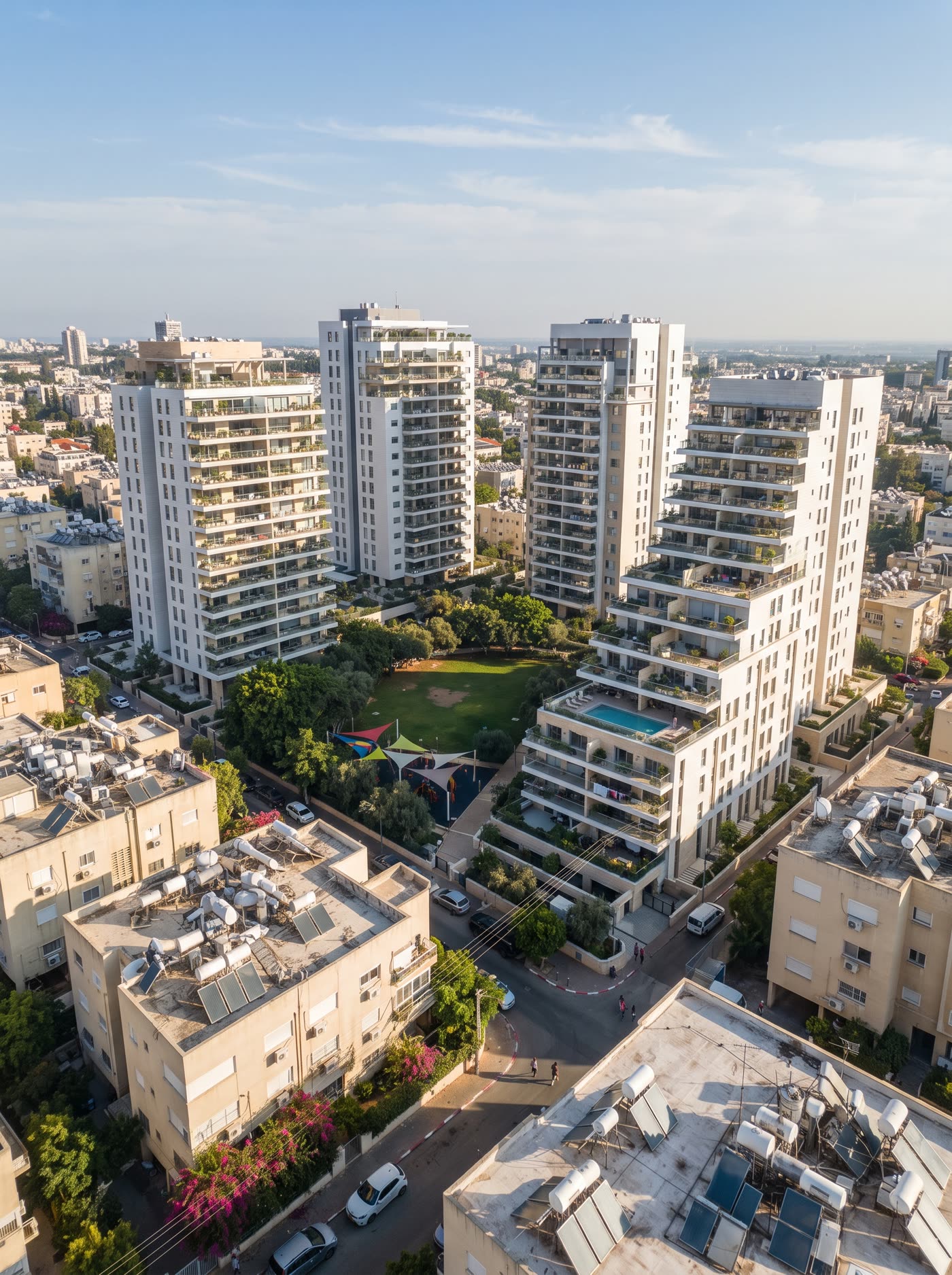 Vue aérienne d’un ensemble de quatre tours résidentielles blanches, avec parc, aire de jeux et piscine, au milieu d’un quartier d’immeubles anciens